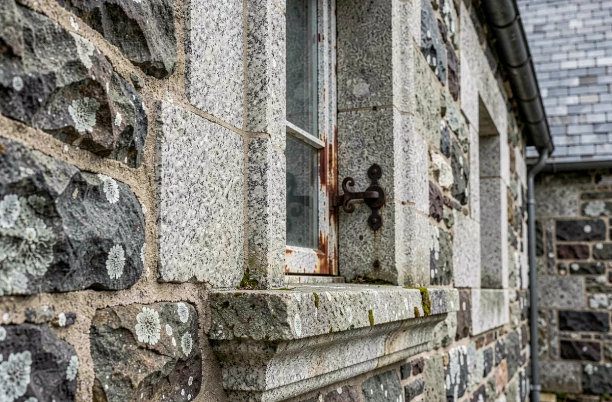 Détail architectural d'encadrement de fenêtre en granite sculpté d'une maison bretonne ancienne avec loquet en fer forgé original, signe de valeur patrimoniale